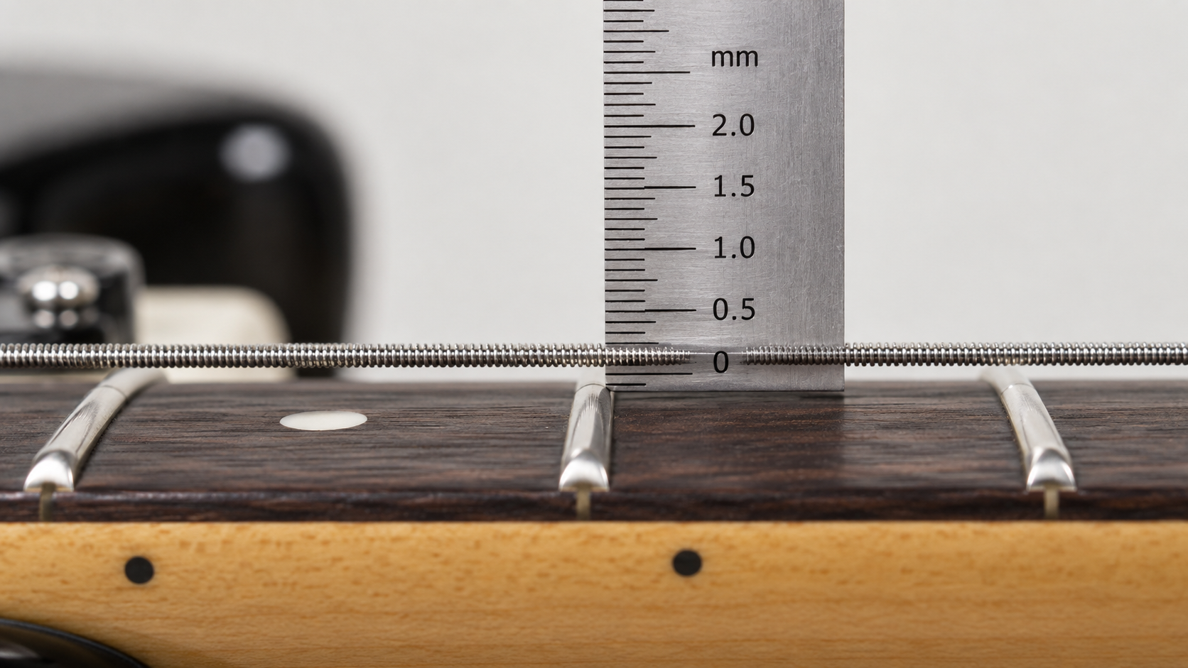 Close-up of a guitar action gauge measuring string height on an electric guitar neck